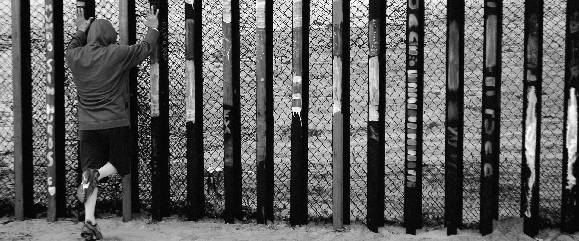Boy all by himself pushes hands against stark border fence