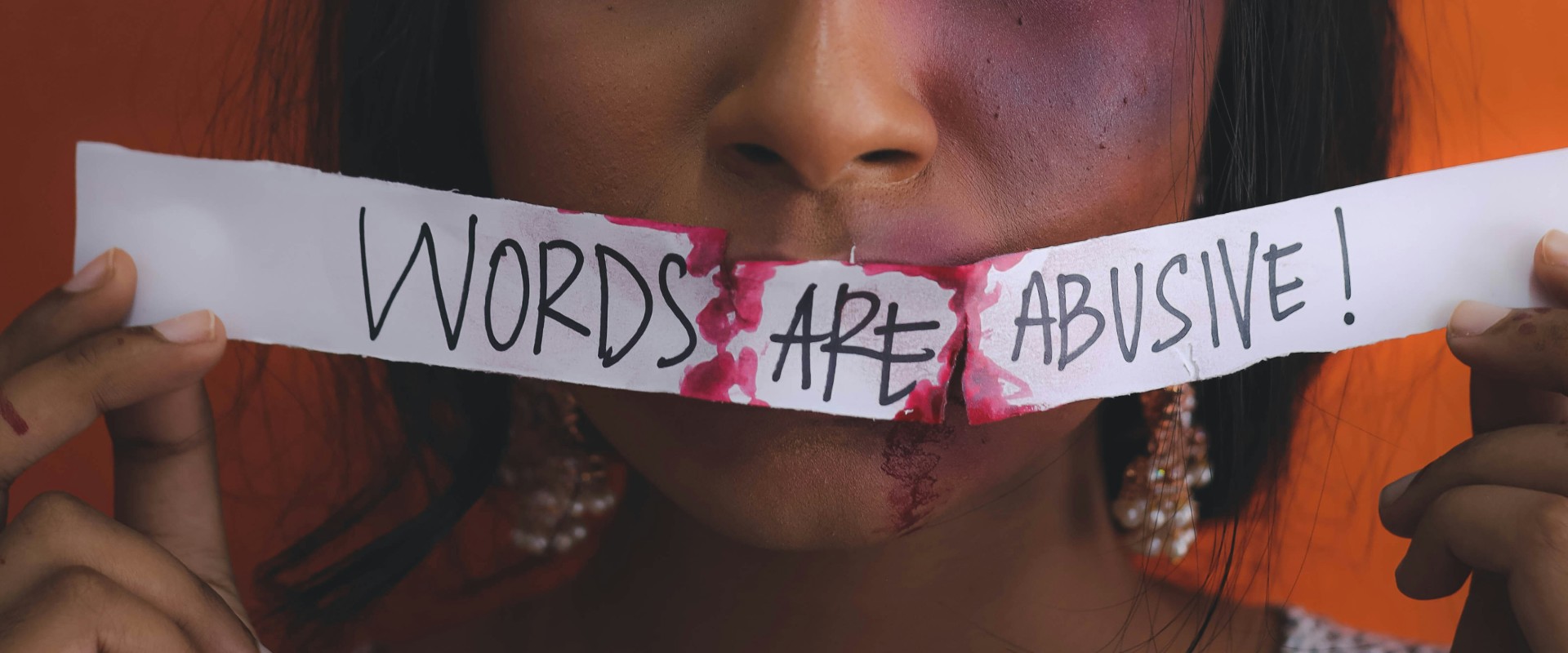 Bruised woman holds tape over her mouth that reads 'words are abuse'